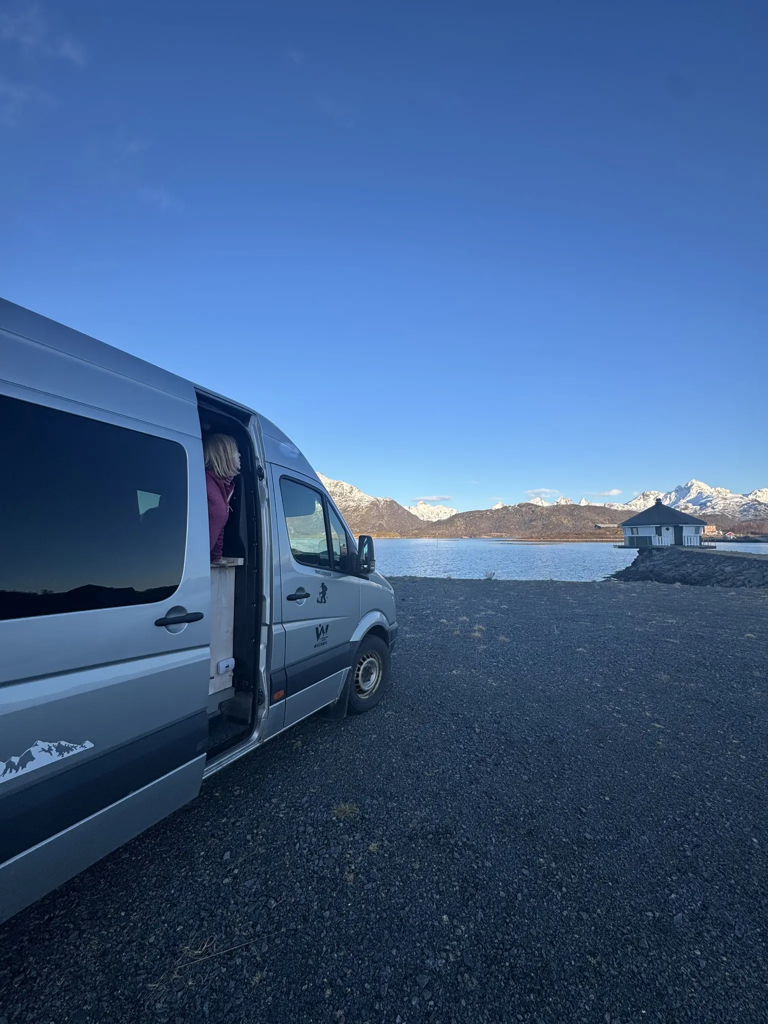 person looking out of a camper van at a snowy mountain lake