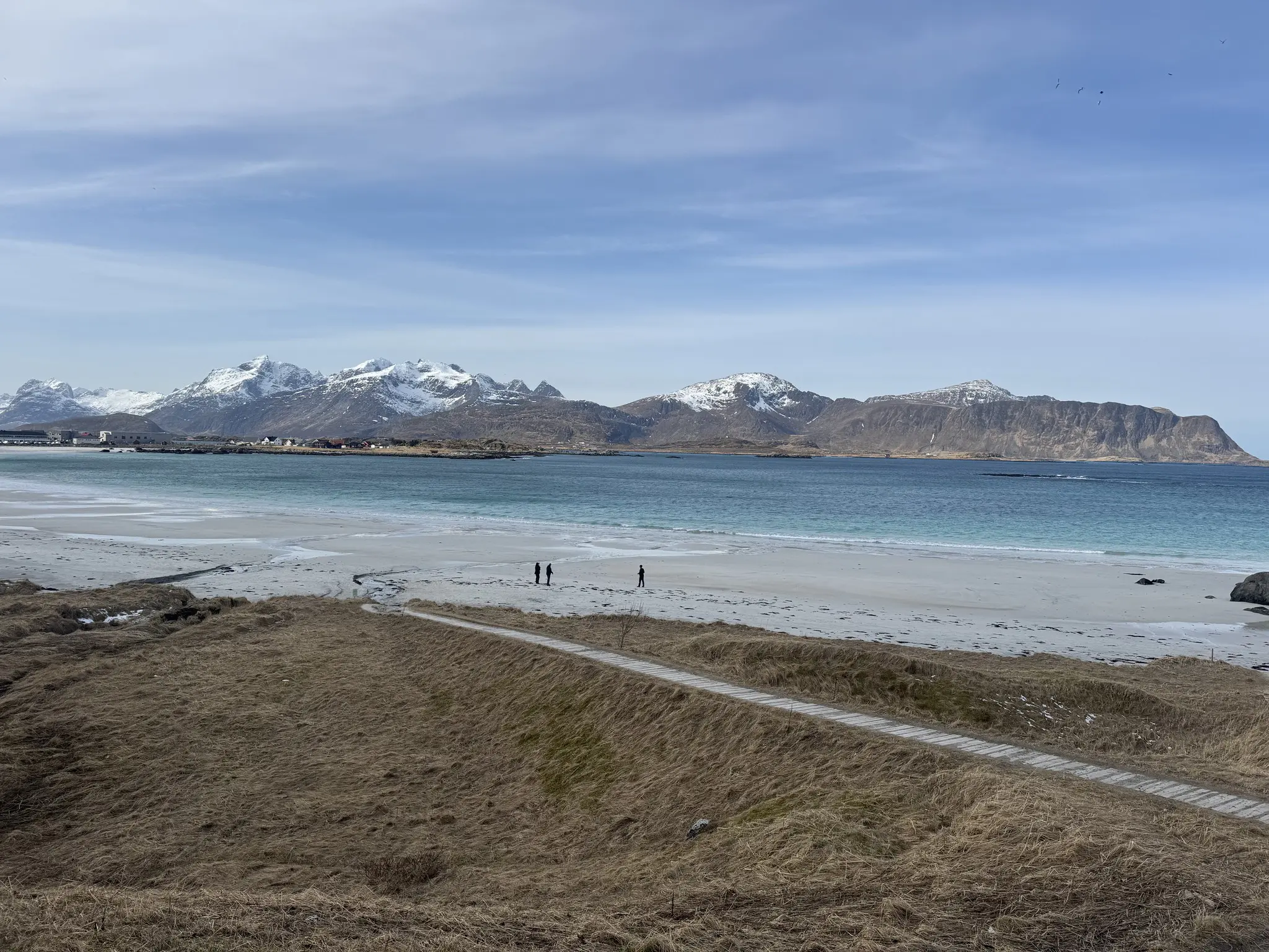 people walking on a white sand beach with snow-capped mountains