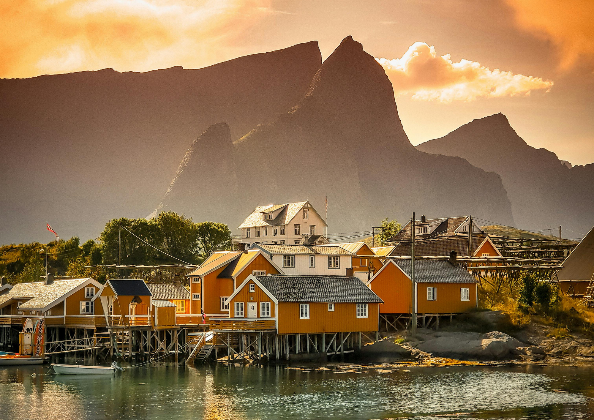 orange fishing huts on stilts by water with mountains at sunset