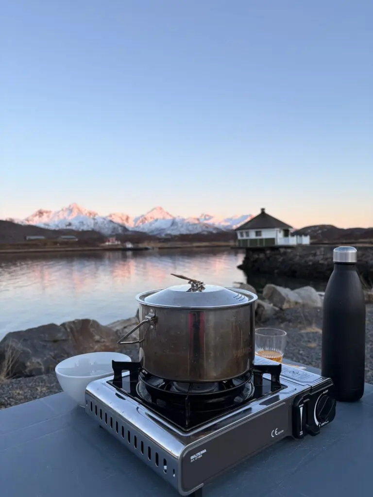 camping stove with pot and bottle by a lake with mountains