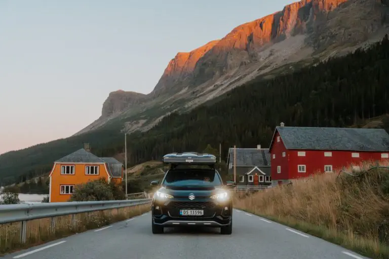 car with rooftop tent driving through a Norwegian village at sunset