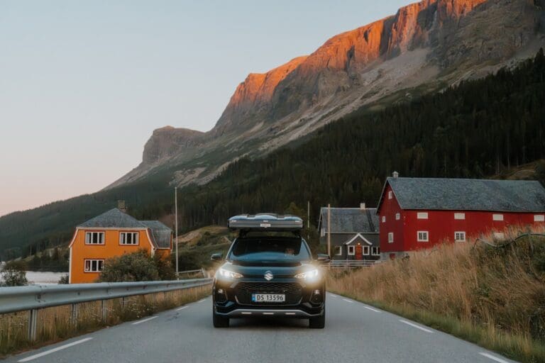 car with rooftop tent driving through a Norwegian village at sunset